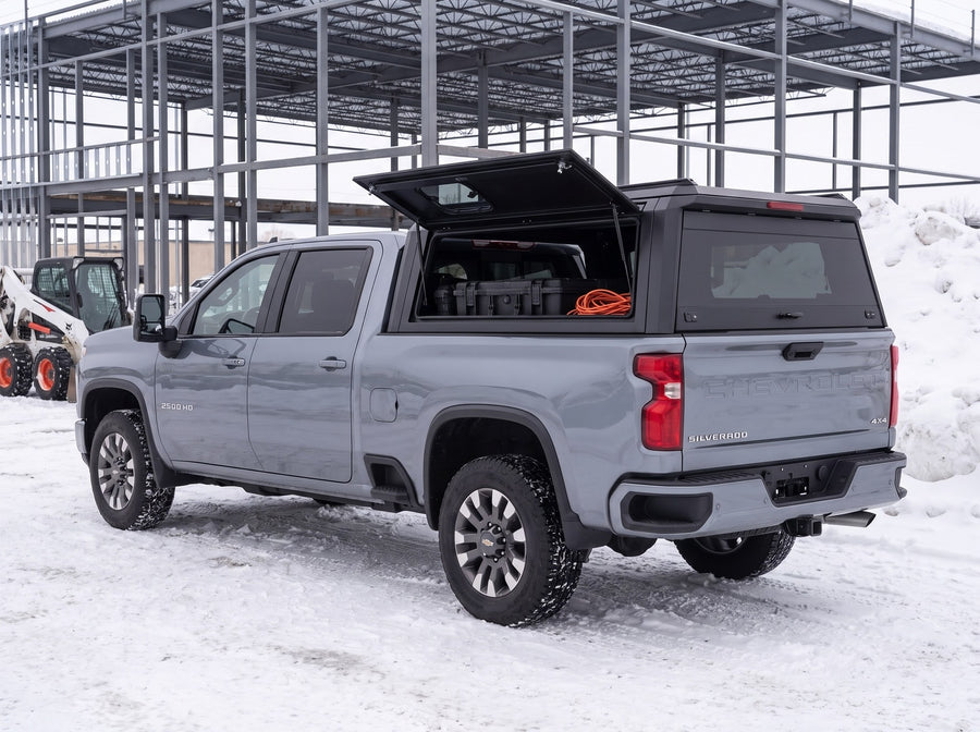 Chevy Silverado 2500HD 3500HD truck cap with the side window lifted open at a snowy job site in winter, tool cases and an extension cord inside