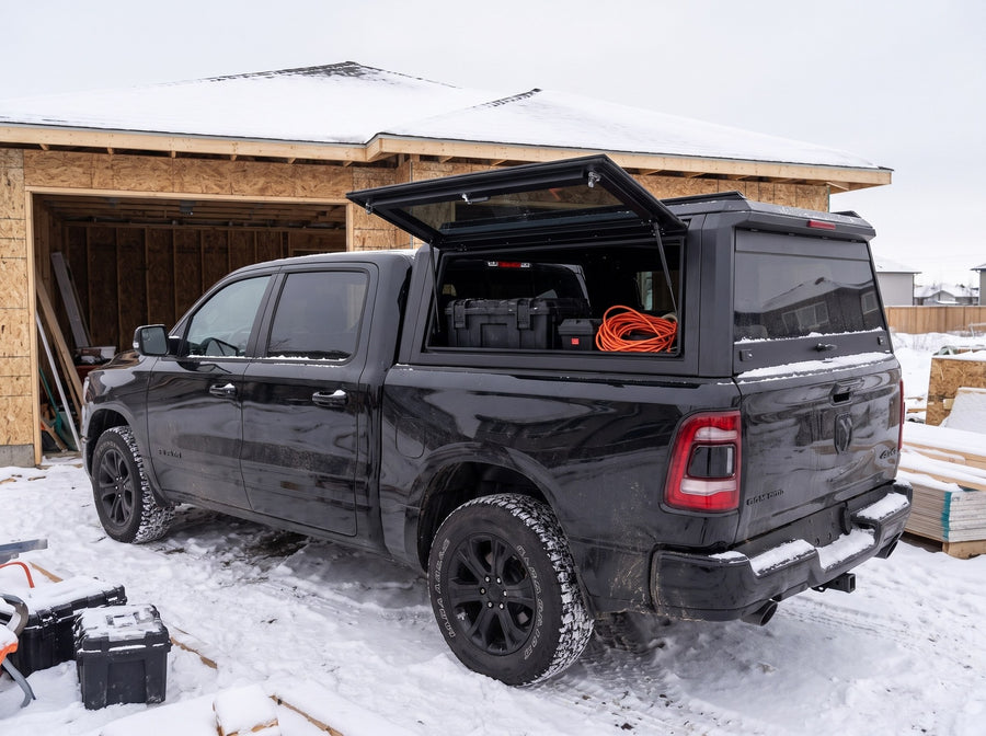 Dodge Ram 1500 truck cap with the side window lifted open at a snowy job site in winter, tool cases and an extension cord inside