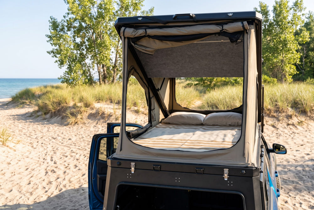 Rear view of the Ford F-150 truck cap camper with the large rear tent window open and the bed made, on a Lake Huron beach