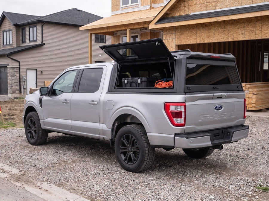 Ford F-150 truck cap with the side window lifted open at a residential job site, tool cases and an extension cord inside