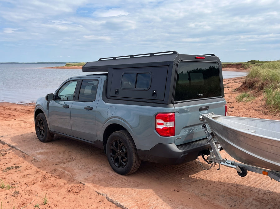 Ford Maverick with a windowed truck cap towing an aluminum fishing boat at a boat launch