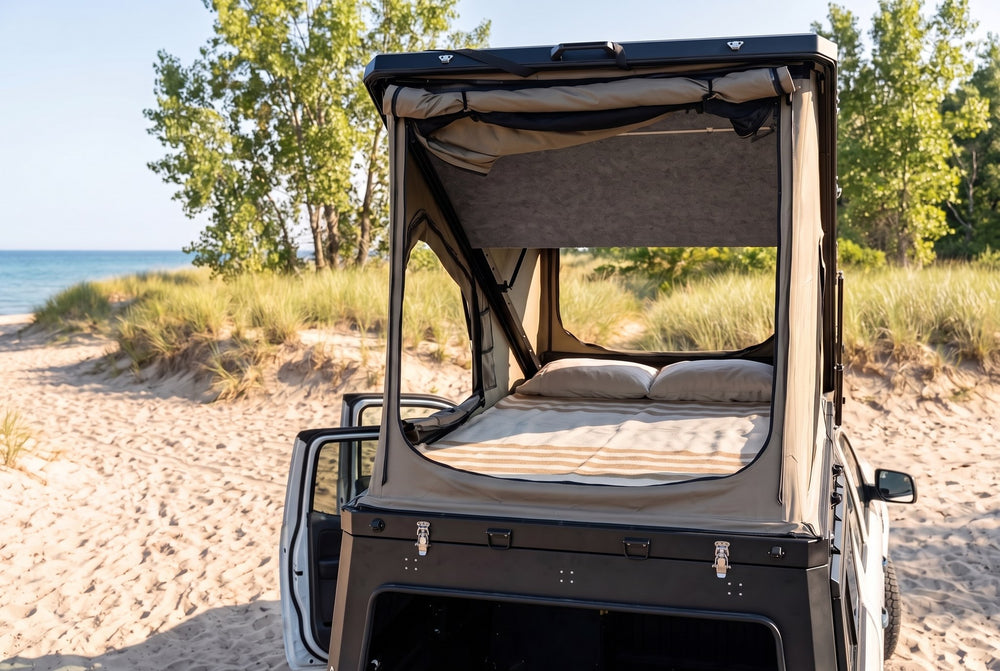 Rear view of the Ford Ranger truck cap camper with the large rear tent window open and the bed made, on a Lake Huron beach