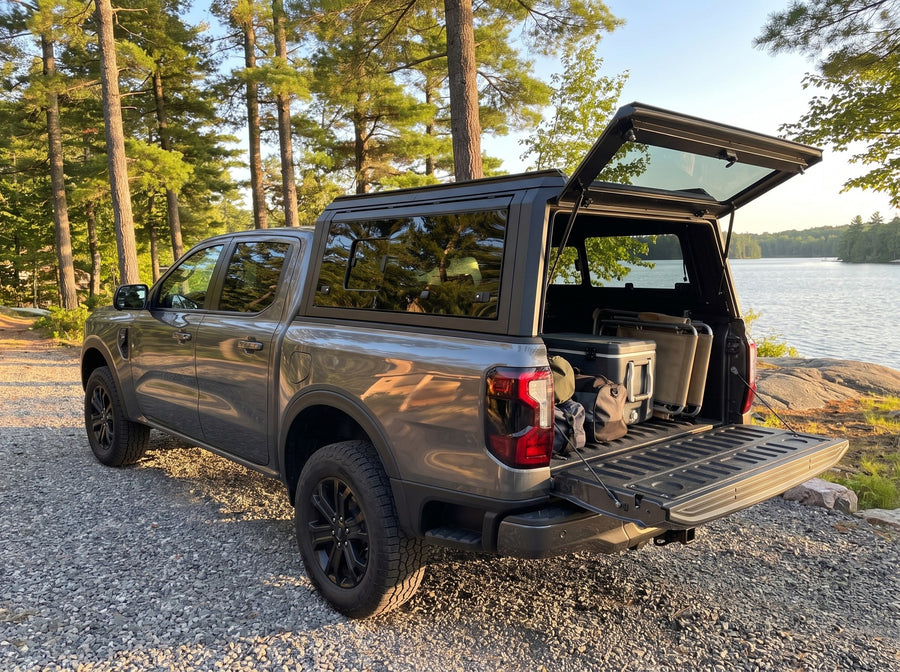 Ford Ranger truck cap open at a cottage with duffel bags, a cooler and a camp chair packed in the bed