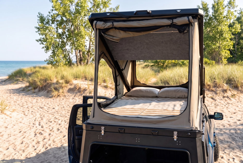 Rear view of the Ram 1500 truck cap camper with the large rear tent window open and the bed made, on a Lake Huron beach