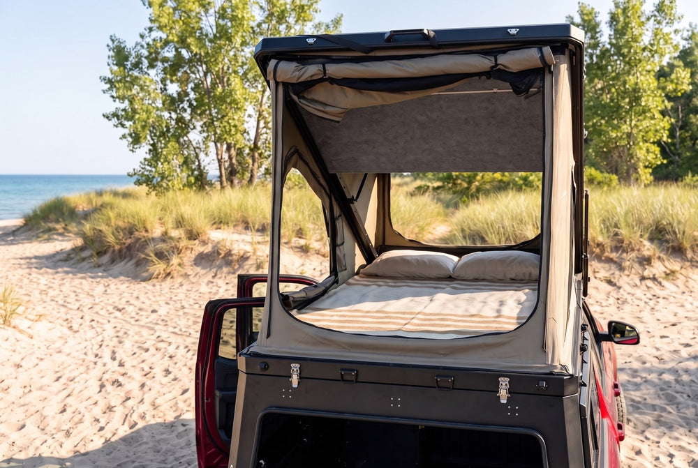 Rear view of the Toyota Tacoma truck cap camper with the large rear tent window open and the bed made, on a Lake Huron beach