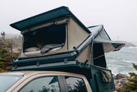 Front pop-up hatch open on the Double Pop-Up truck cap camper above a Chevy Colorado cab, with the bed made inside