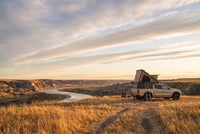 Wide view of a Chevy Colorado pop-up truck cap camper camped above an Alberta badlands river valley in evening light