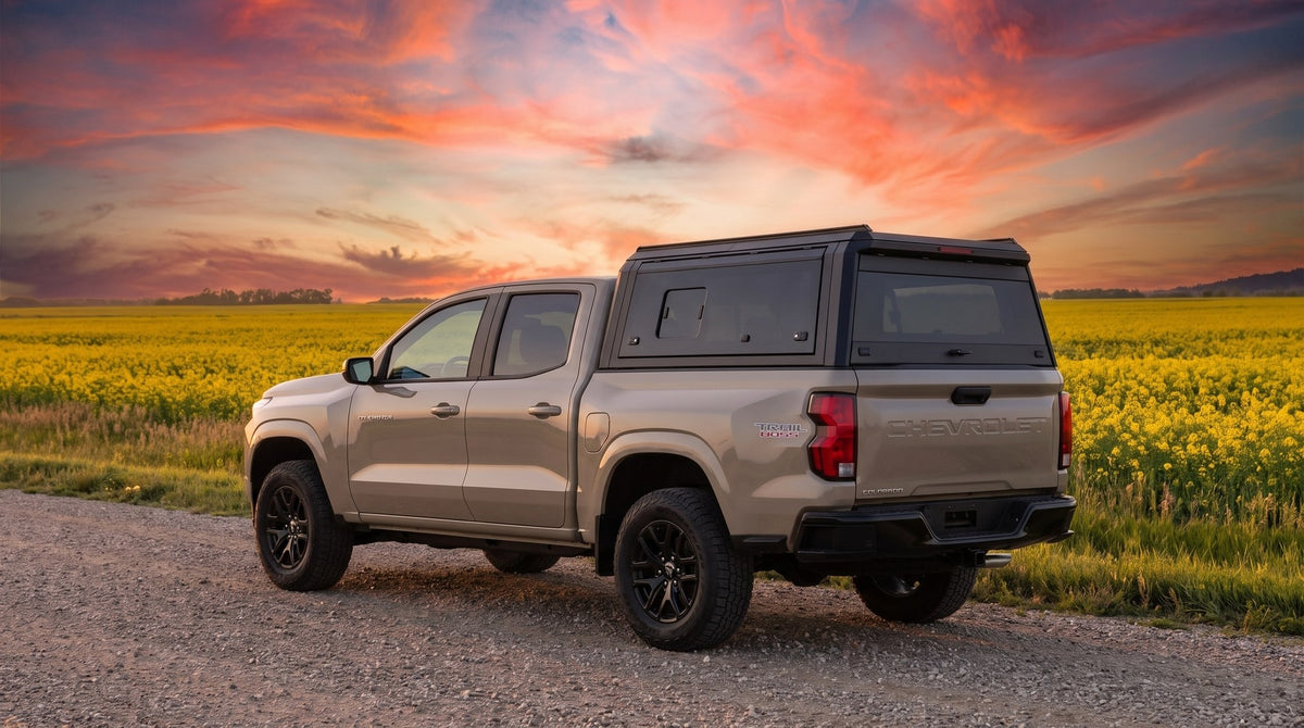 Wide view of a Chevy Colorado with a windowed aluminum truck cap parked at a gravel road across the Manitoba prairie at sunset in late summer