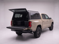Rear door of the Chevy Colorado truck cap lifted open with the tailgate down and storage totes in the bed
