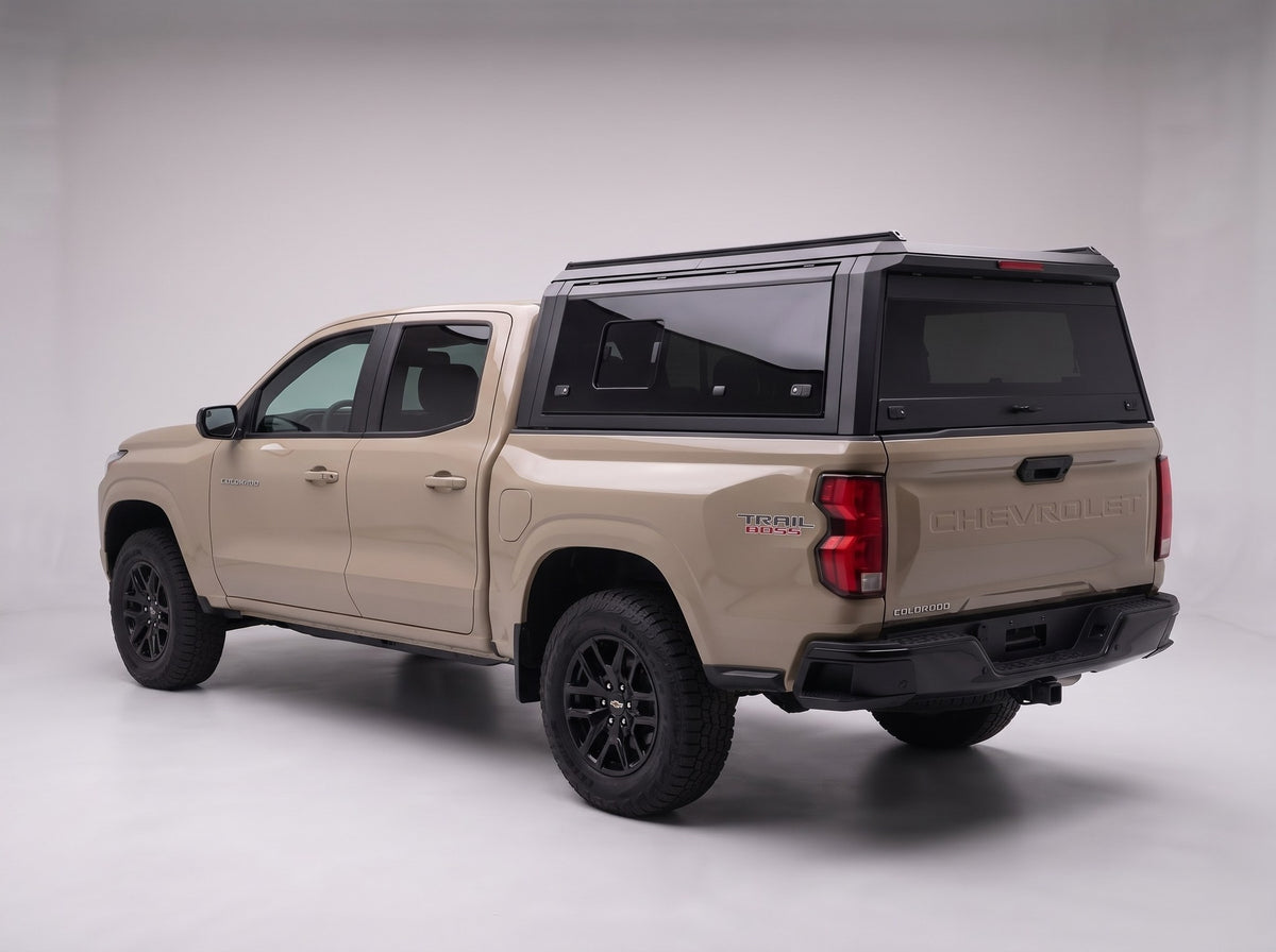 Matte black aluminum truck cap with tinted windows on a Chevy Colorado, studio rear three-quarter view