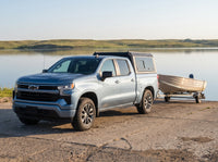 Chevy Silverado 1500 with a windowed truck cap towing an aluminum fishing boat at a boat launch