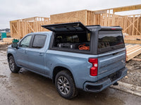 Chevy Silverado 1500 truck cap with the side window lifted open at a job site, tool cases and an extension cord inside
