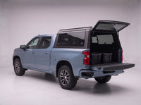 Rear door of the Chevy Silverado 1500 truck cap lifted open with the tailgate down and storage totes in the bed