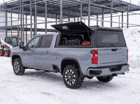 Chevy Silverado 2500HD 3500HD truck cap with the side window lifted open at a snowy job site in winter, tool cases and an extension cord inside