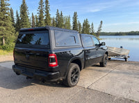 Dodge Ram 1500 with a windowed truck cap towing an aluminum fishing boat at a boat launch