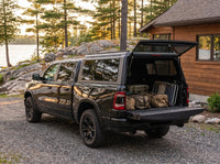 Dodge Ram 1500 truck cap open at a cottage with duffel bags, a cooler and a camp chair packed in the bed