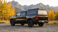 Wide view of a Dodge Ram 1500 with a windowed aluminum truck cap parked at a gravel pull-off in the Kananaskis foothills of Alberta in autumn