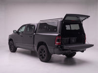 Rear door of the Dodge Ram 1500 truck cap lifted open with the tailgate down and storage totes in the bed