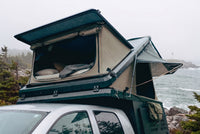 Front pop-up hatch open on the Double Pop-Up truck cap camper above a Dodge Ram 2500/3500 cab, with the bed made inside