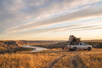 Wide view of a Dodge Ram 2500/3500 pop-up truck cap camper camped above an Alberta badlands river valley in evening light
