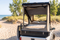 Rear view of the Dodge Ram 2500/3500 truck cap camper with the large rear tent window open and the bed made, on a Lake Huron beach