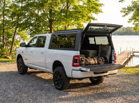 Dodge Ram 2500 3500 truck cap open at a cottage with duffel bags, a cooler and a camp chair packed in the bed