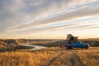 Wide view of a Ford F-150 pop-up truck cap camper camped above an Alberta badlands river valley in evening light