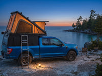 Ford F-150 pop-up truck cap camper glowing at dusk on the Georgian Bay shore with camp chairs and a lantern