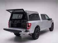 Rear door of the Ford F-150 truck cap lifted open with the tailgate down and storage totes in the bed