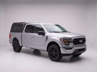 Front three-quarter view of a silver Ford F-150 with the black aluminum truck cap behind the cab