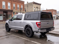 Silver Ford F-150 with a black truck cap with windows parked on a small-town Ontario main street after rain