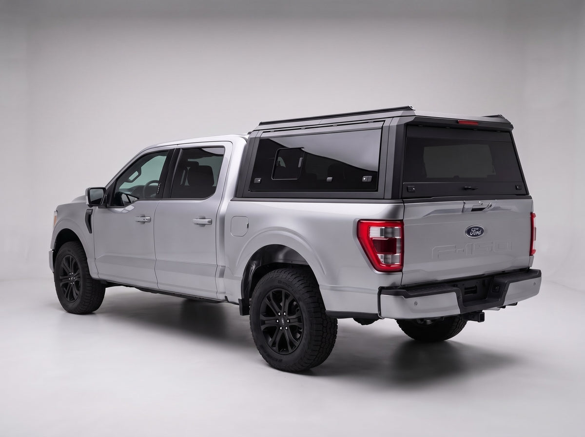 Matte black aluminum truck cap with tinted windows on a silver Ford F-150, studio rear three-quarter view