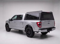 Matte black aluminum truck cap with tinted windows on a silver Ford F-150, studio rear three-quarter view