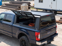 Ford F-250 F-350 Super Duty truck cap with the side window lifted open at a job site, tool cases and an extension cord inside