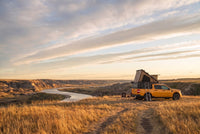 Wide view of a Ford Maverick pop-up truck cap camper camped above an Alberta badlands river valley in evening light