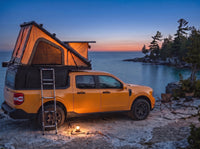 Ford Maverick pop-up truck cap camper glowing at dusk on the Georgian Bay shore with camp chairs and a lantern