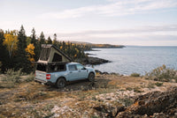 Wide view of a Ford Maverick truck camper set up above the Lake Superior shoreline in autumn