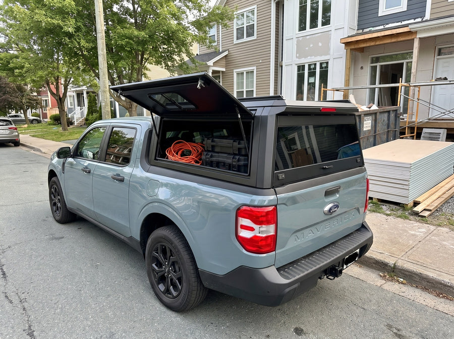 Ford Maverick truck cap with the side window lifted open at a job site, tool cases and an extension cord inside