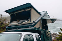 Front pop-up hatch open on the Double Pop-Up truck cap camper above a Ford Ranger cab, with the bed made inside