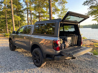 Ford Ranger truck cap open at a cottage with duffel bags, a cooler and a camp chair packed in the bed