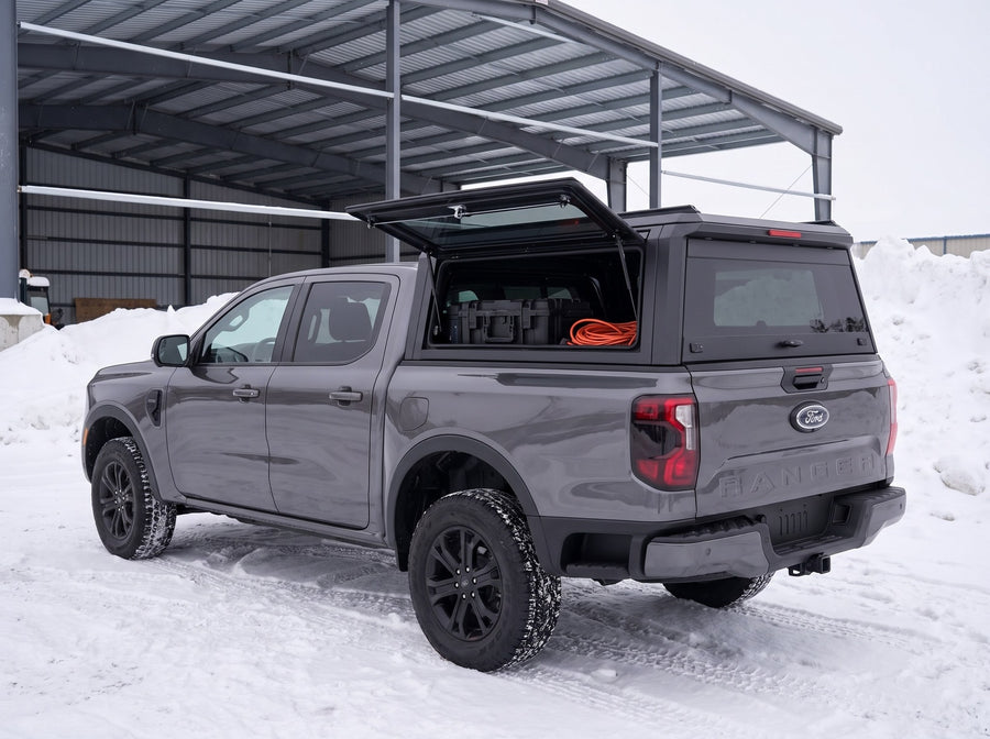 Ford Ranger truck cap with the side window lifted open at a snowy job site in winter, tool cases and an extension cord inside