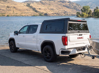 GMC Sierra 1500 with a windowed truck cap towing an aluminum fishing boat at a boat launch
