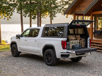 GMC Sierra 1500 truck cap open at a cottage with duffel bags, a cooler and a camp chair packed in the bed