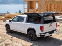 GMC Sierra 1500 truck cap with the side window lifted open at a job site, tool cases and an extension cord inside