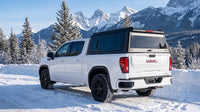 Wide view of a GMC Sierra 1500 with a windowed aluminum truck cap parked at a snow-covered mountain highway pull-off in the BC Rockies in winter
