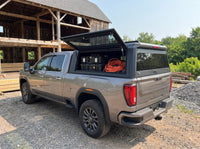 GMC Sierra 2500HD 3500HD truck cap with the side window lifted open at a job site, tool cases and an extension cord inside