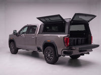 Rear door of the GMC Sierra 2500HD 3500HD truck cap lifted open with the tailgate down and storage totes in the bed