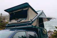 Front pop-up hatch open on the Double Pop-Up truck cap camper above a Ram 1500 cab, with the bed made inside