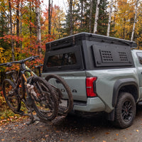 Toyota Tacoma canopy camper closed, rear three-quarter view showing the locking MOLLE side panel and hitch bike rack