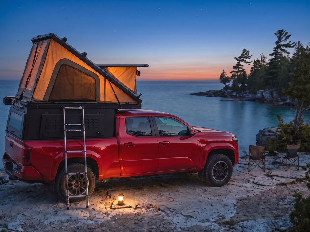Toyota Tacoma pop-up truck cap camper glowing at dusk on the Georgian Bay shore with camp chairs and a lantern